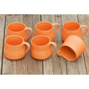 Puede incluir: Seis tazas de terracota con un diseño acanalado. Las tazas están dispuestas en semicírculo sobre una superficie de madera.