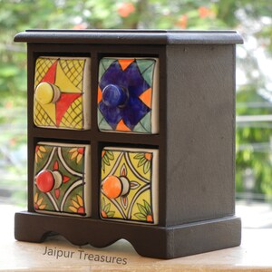 May include: A small wooden box with six colorful ceramic drawers. Each drawer has a different pattern and a knob. The box is on a wooden surface. Jaipur Treasures.