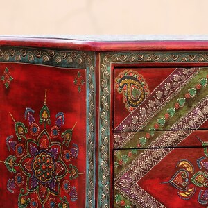 May include: A red wooden chest with hand-painted floral designs in shades of green, blue, yellow, and purple. The chest has three drawers with ornate handles.