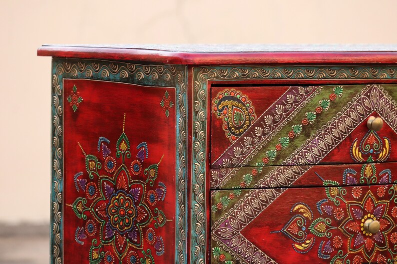 May include: A red wooden chest with hand-painted floral designs in shades of green, blue, yellow, and purple. The chest has three drawers with ornate handles.