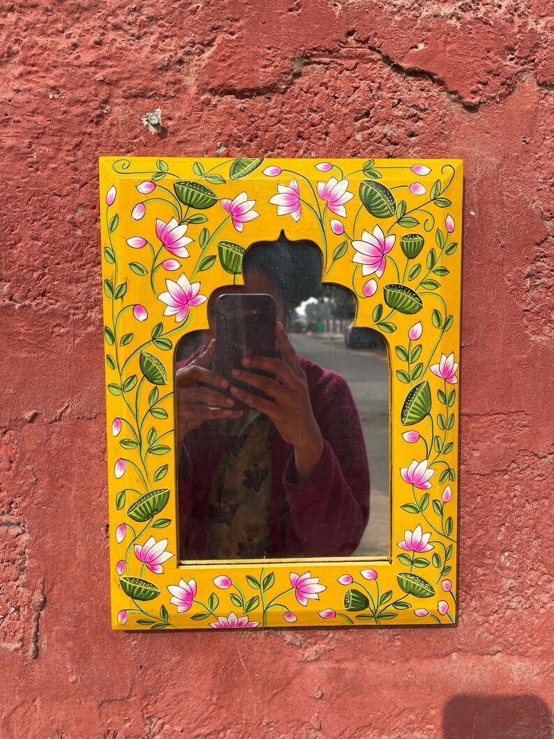 Puede incluir: Un espejo de madera amarillo con un dise&ntilde;o floral pintado a mano con flores rosas y hojas verdes. El espejo tiene un arco decorativo en la parte superior.