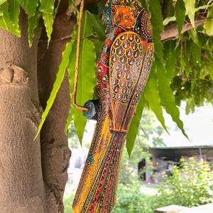 May include: A colorful wooden bird ornament with intricate details and a hanging loop. The bird is painted in shades of yellow, orange, red, blue, green, and black.