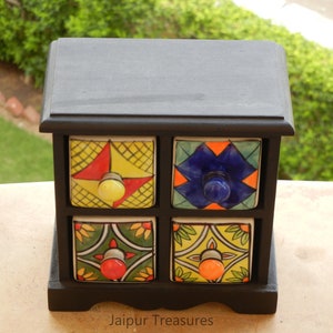 May include: A black wooden box with four small drawers. Each drawer has a colorful ceramic front with a different geometric pattern and a knob. The box is labeled "Jaipur Treasures".