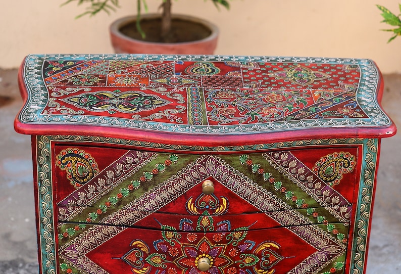 May include: A red wooden chest with three drawers, each decorated with intricate hand-painted floral and paisley designs in vibrant colors like green, gold, and blue.
