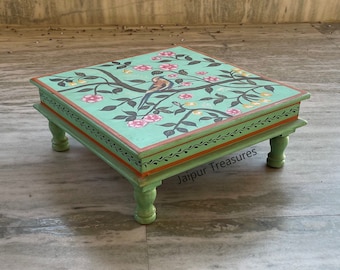 May include: A hand-painted wooden table with a green base and a floral design featuring a bird on a branch. The table has four legs and a square top. The design includes pink flowers, green leaves, and a gold bird. The table is labeled "Jaipur Treasures".
