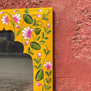 Puede incluir: Un espejo de madera amarillo con un dise&ntilde;o floral pintado a mano. El marco presenta flores rosas, hojas verdes y detalles amarillos.