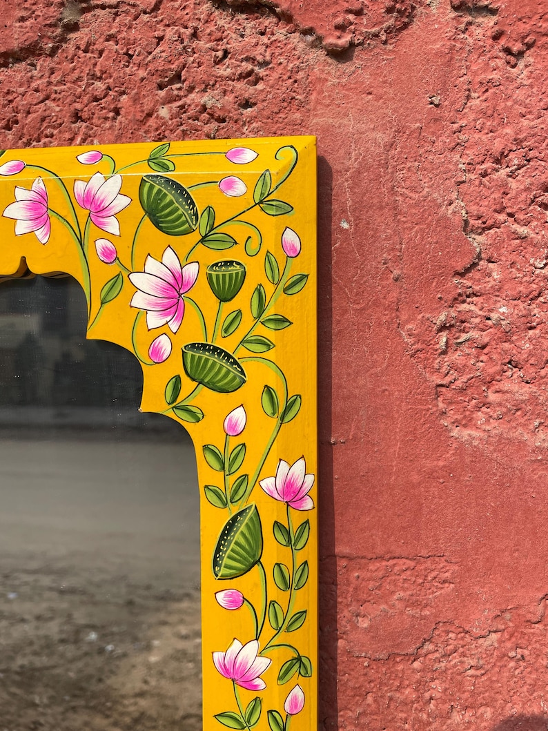 Puede incluir: Un espejo de madera amarillo con un dise&ntilde;o floral pintado a mano. El marco presenta flores rosas, hojas verdes y detalles amarillos.
