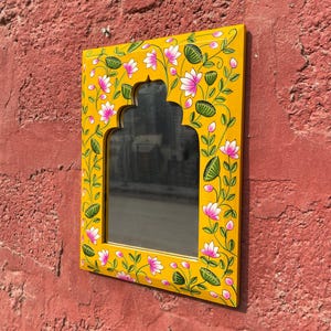 Puede incluir: Un espejo de madera amarillo con un dise&ntilde;o floral pintado a mano. El espejo tiene una forma de arco tradicional y est&aacute; decorado con flores rosas y hojas verdes.