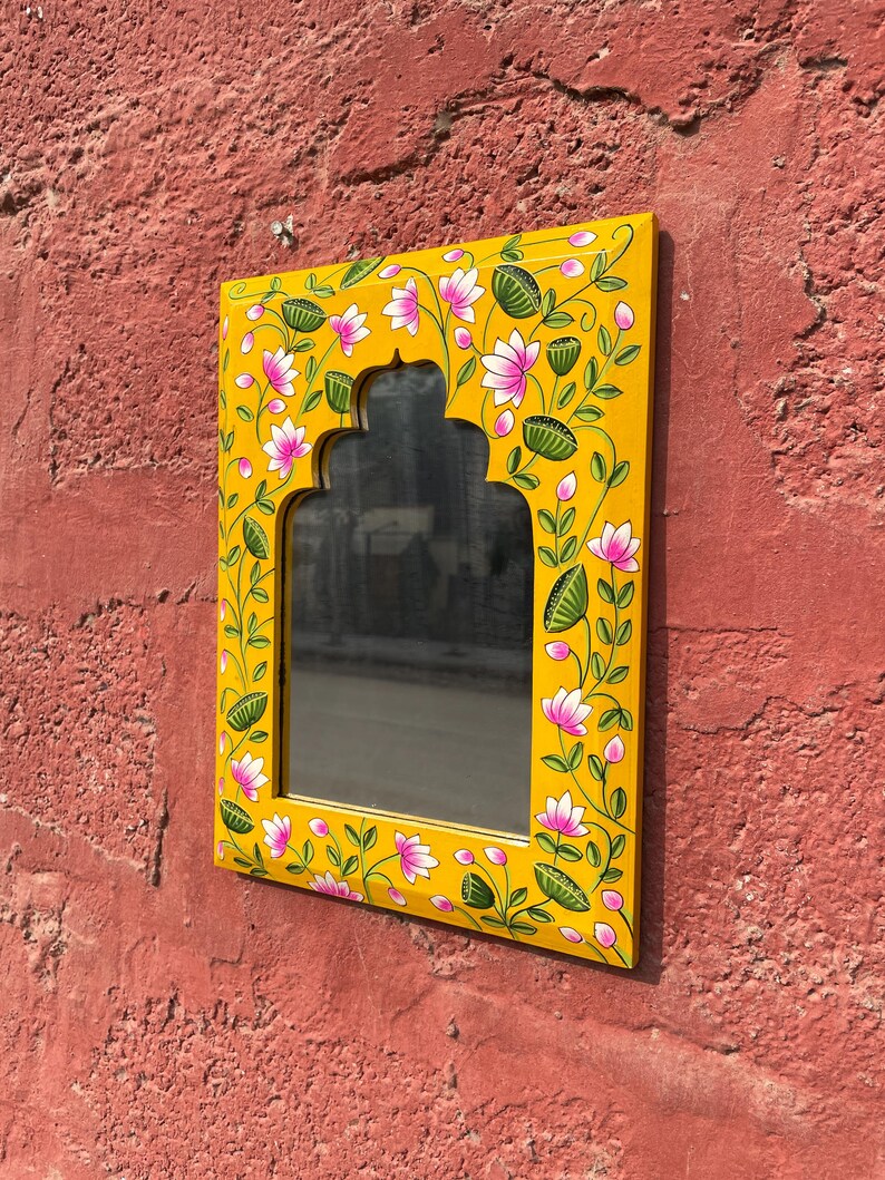 Puede incluir: Un espejo de madera amarillo con un dise&ntilde;o floral pintado a mano. El espejo tiene una forma de arco tradicional y est&aacute; decorado con flores rosas y hojas verdes.