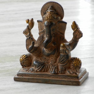 Puede incluir: Una estatua de Ganesha negra y dorada con una base decorativa. La estatua est&aacute; sentada sobre una superficie de m&aacute;rmol blanco.