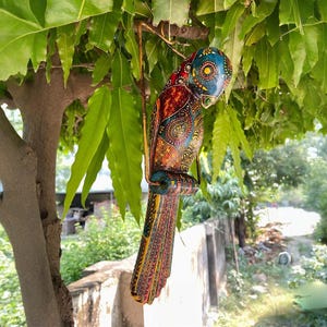 May include: A colorful wooden parrot with intricate painted details, hanging from a branch. The parrot is painted in shades of blue, green, red, yellow, and orange.