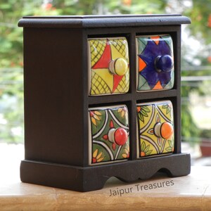 May include: A black wooden box with four small drawers. Each drawer has a colorful ceramic front with a different pattern. The box is labeled "Jaipur Treasures".