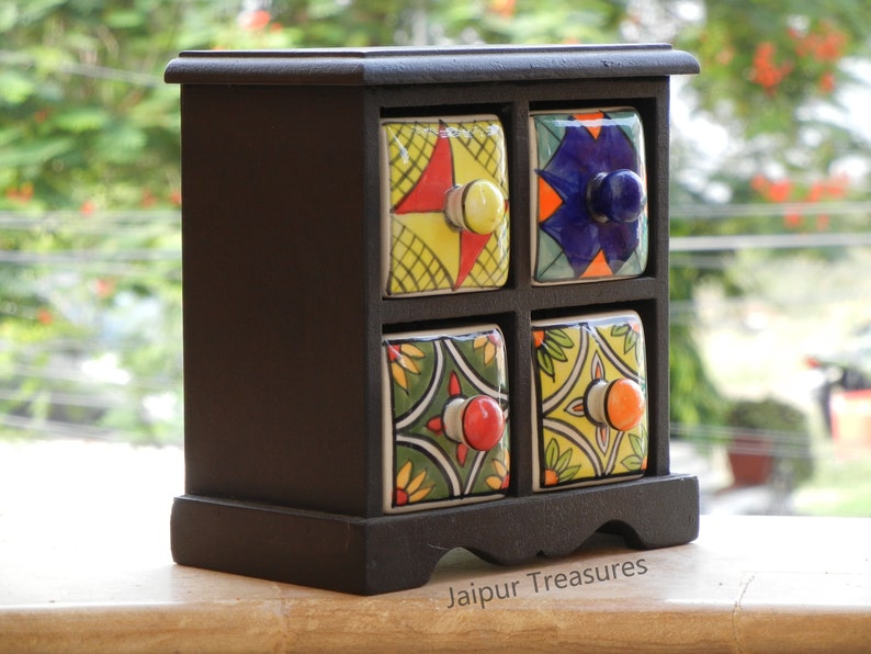 May include: A black wooden box with four small drawers. Each drawer has a colorful ceramic front with a different pattern. The box is labeled "Jaipur Treasures".