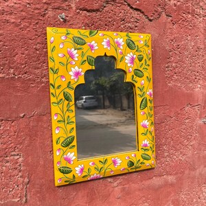 Puede incluir: Un espejo de madera amarillo con un dise&ntilde;o floral pintado a mano. El espejo tiene una forma de arco tradicional y est&aacute; decorado con flores rosas y hojas verdes.