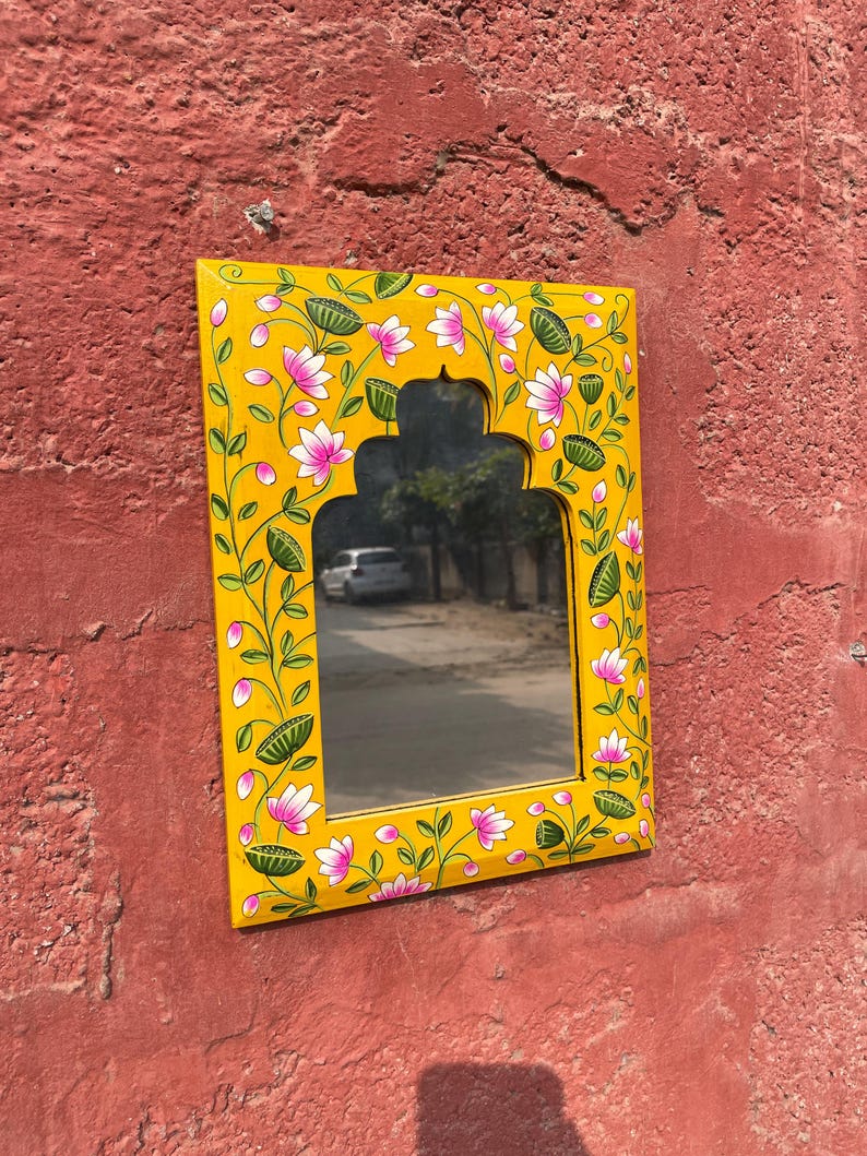 Puede incluir: Un espejo de madera amarillo con un dise&ntilde;o floral pintado a mano. El espejo tiene una forma de arco tradicional y est&aacute; decorado con flores rosas y hojas verdes.
