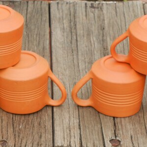 May include: Six terracotta mugs stacked in two groups of three. The mugs are a light orange color and have a textured surface.