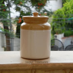 May include: A white ceramic jar with a brown lid. The jar has a simple design and is perfect for storing spices, tea, or other small items. The jar is labeled "Jaipur Treasures".