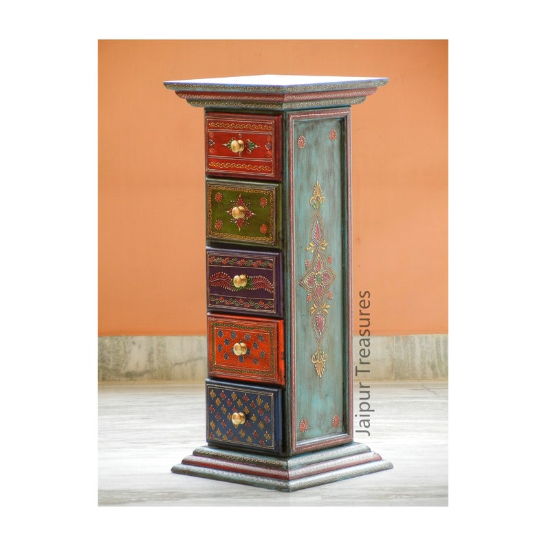 K&ouml;nnte beinhalten: Eine hohe, schmale Holzkiste mit f&uuml;nf Schubladen. Jede Schublade ist in einer anderen leuchtenden Farbe mit kunstvollen Designs und goldenen Akzenten bemalt. Die Kiste ist hellblau mit goldenen Akzenten bemalt und die Worte "Jaipur Treasures" sind auf der Seite aufgedruckt.