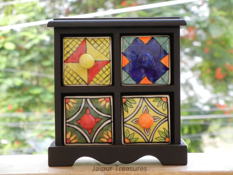 May include: A black wooden box with four small drawers. Each drawer has a colorful ceramic front with a different geometric pattern and a knob. The box is labeled "Jaipur Treasures".
