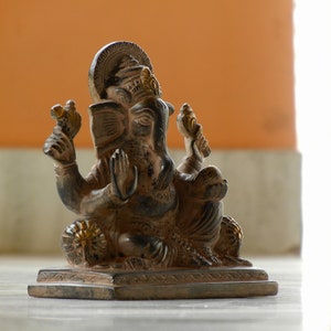 Puede incluir: Una estatua negra y dorada del dios hind&uacute; Ganesha, sentado sobre una base con un borde decorativo. La estatua est&aacute; intrincadamente detallada y tiene un dise&ntilde;o tradicional.