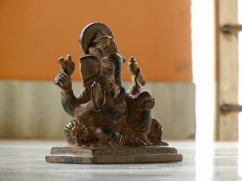 Puede incluir: Una estatua negra y dorada del dios hind&uacute; Ganesha, sentado sobre una base con un borde decorativo. La estatua est&aacute; intrincadamente detallada y tiene un dise&ntilde;o tradicional.