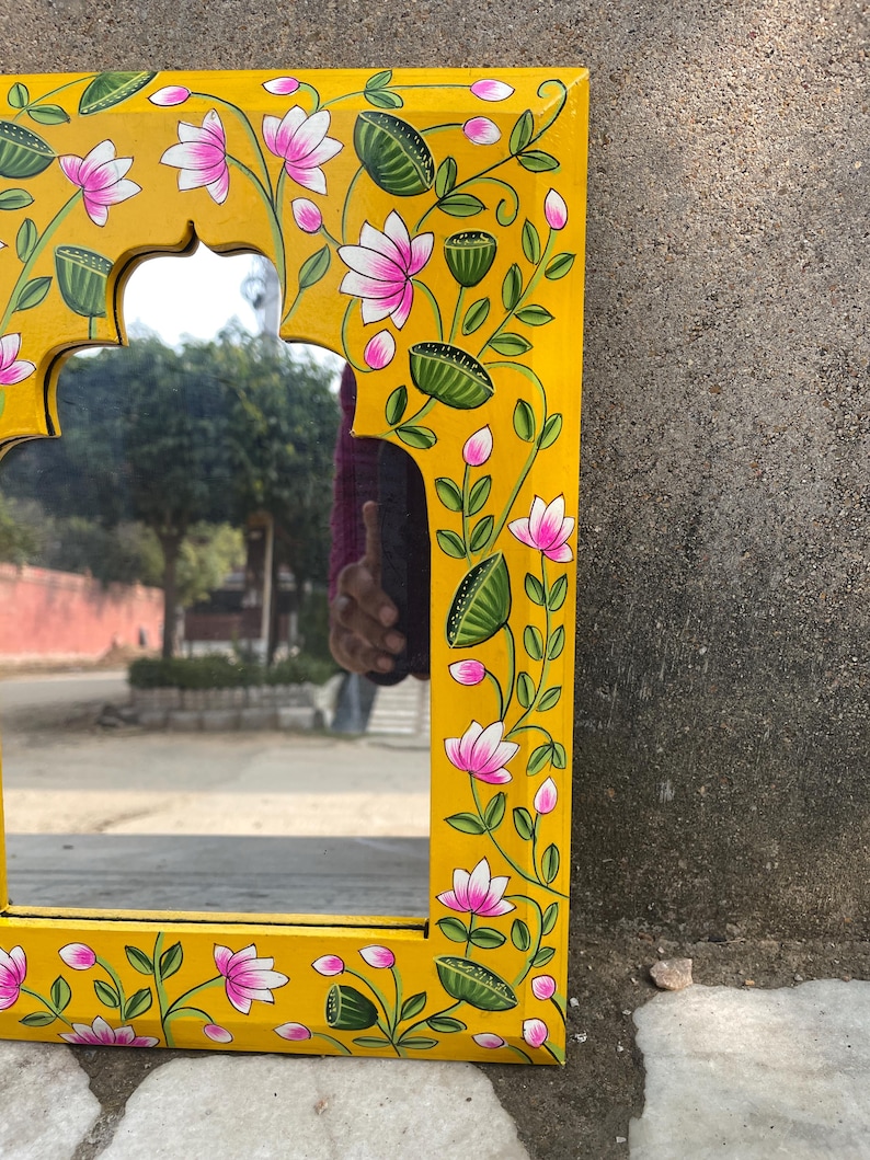 Puede incluir: Un espejo de madera amarillo con un dise&ntilde;o floral pintado a mano. El espejo tiene una forma de arco tradicional y est&aacute; decorado con flores rosas y hojas verdes.