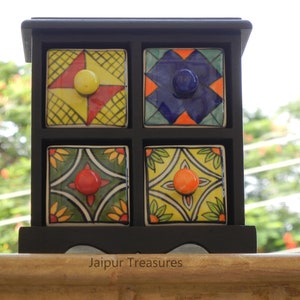 May include: A black wooden box with four small drawers. Each drawer has a colorful ceramic front with a different geometric pattern and a knob. The box is sitting on a wooden surface. Jaipur Treasures.