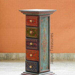 K&ouml;nnte beinhalten: Eine tealblaue Holzkiste mit f&uuml;nf Schubladen. Jede Schublade ist mit einem anderen bunten Design bemalt und hat einen Messingknopf. Die Kiste ist mit Goldfarbe verziert und tr&auml;gt den Schriftzug "Jaipur Treasures".