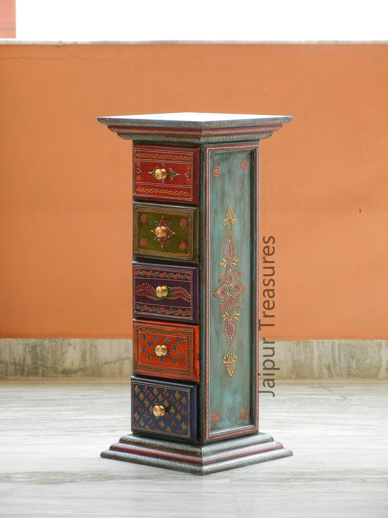 K&ouml;nnte beinhalten: Eine tealblaue Holzkiste mit f&uuml;nf Schubladen. Jede Schublade ist mit einem anderen bunten Design bemalt und hat einen Messingknopf. Die Kiste ist mit Goldfarbe verziert und tr&auml;gt den Schriftzug "Jaipur Treasures".