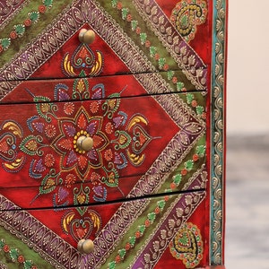 May include: A red wooden chest of drawers with intricate hand-painted floral designs in shades of green, purple, gold, and yellow. The drawers have brass knobs.