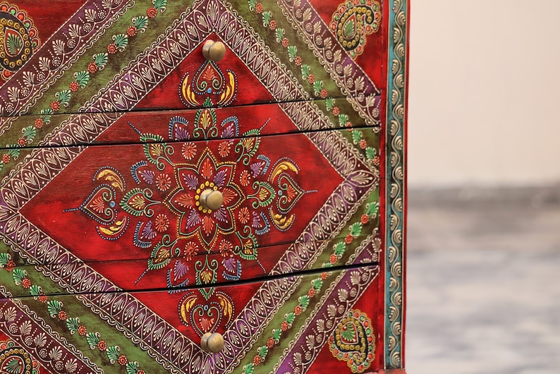 May include: A red wooden chest of drawers with intricate hand-painted floral designs in shades of green, purple, gold, and yellow. The drawers have brass knobs.