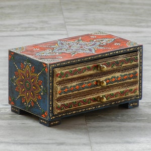 Puede incluir: Una peque&ntilde;a caja de madera con tres cajones, pintada en azul, naranja y dorado con intrincados dise&ntilde;os florales. La caja tiene pomos de lat&oacute;n en los cajones.