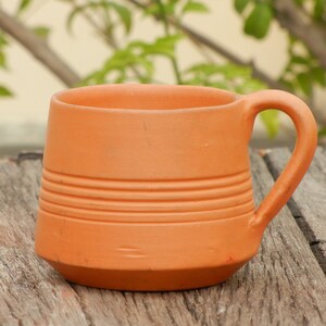 May include: A terracotta mug with a handle. The mug has a brown glaze and is decorated with horizontal lines.