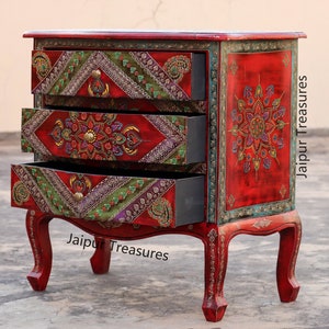 May include: A red wooden chest of drawers with three drawers. The drawers are decorated with colorful floral and geometric patterns. The chest is on a gray surface. "Jaipur Treasures" is written on the front of the chest.