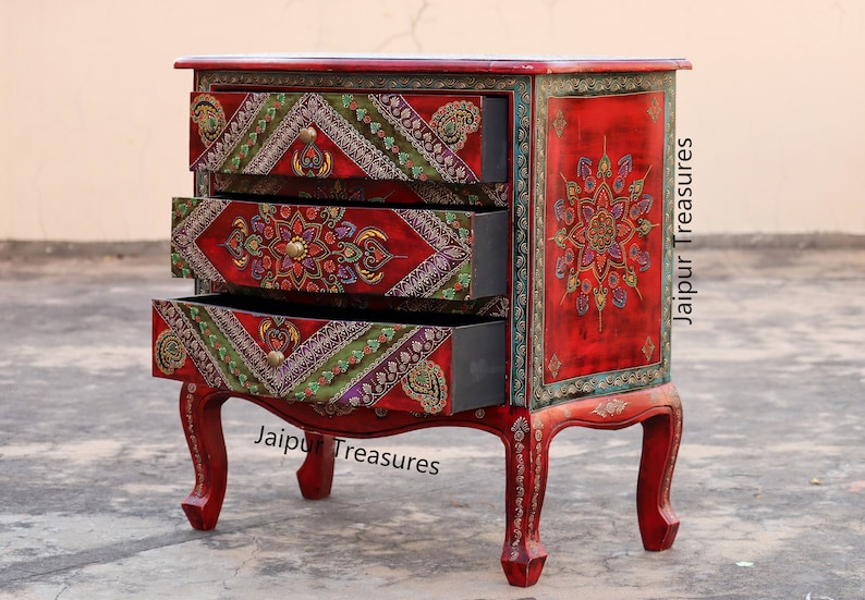 May include: A red wooden chest of drawers with three drawers. The drawers are decorated with colorful floral and geometric patterns. The chest is on a gray surface. "Jaipur Treasures" is written on the front of the chest.