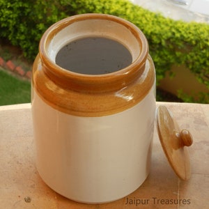 May include: A white ceramic jar with a brown lid and a brown band around the top. The jar is empty and the lid is off.
