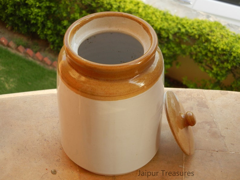 May include: A white ceramic jar with a brown lid and a brown band around the top. The jar is empty and the lid is off.
