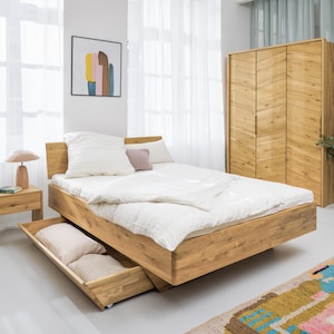 Peut inclure: Un lit en bois clair avec une table de chevet et une armoire assorties. Le lit a un profil bas et un tiroir coulissant. Le lit est fait avec une literie et des oreillers blancs. Une peinture abstraite colorée est accrochée au mur. Le lit mesure environ 200 cm de long.