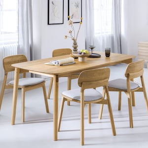 Könnte beinhalten: Ein Esstisch aus hellem Holz mit vier passenden Stühlen. Die Stühle haben grau gepolsterte Sitze und geschwungene Rückenlehnen. Der Tisch ist mit einer Vase mit Blumen, Obst und Glaswaren gedeckt.