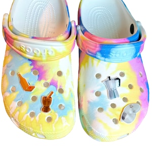 May include: A pair of tie-dye Crocs with colorful Jibbitz charms. The charms include a bottle of wine, a mortar and pestle, a coffee pot, and a measuring cup.