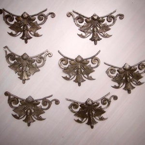 Può includere: Sette ornamenti in metallo decorati con un motivo floreale. Ogni pezzo presenta un motivo centrale di un fiore stilizzato con foglie e volute.