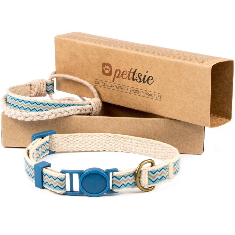 May include: A blue and brown patterned cat collar with a blue buckle and a gold metal D-ring. The collar is packaged in a brown cardboard box with the text "pettsie" and "CAT COLLAR WITH FRIENDSHIP BRACELET".