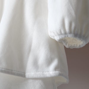 May include: White velvet dress with long sleeves and a gathered hem.
