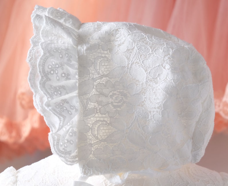May include: White lace bonnet with a ruffled edge. The bonnet is made of delicate lace and has a soft, feminine look.