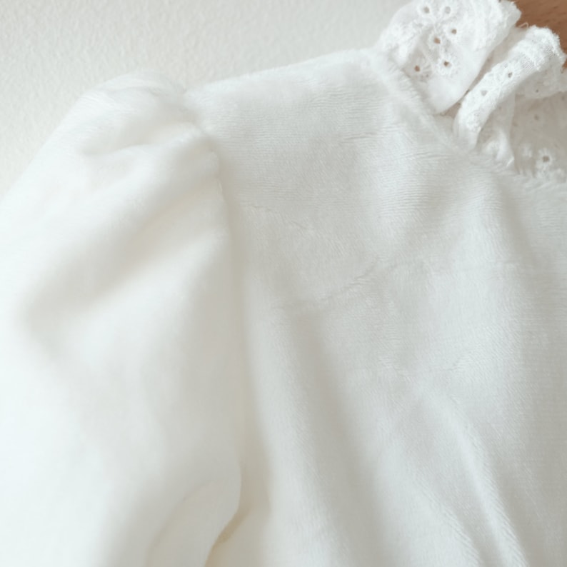 May include: White long-sleeved blouse with a ruffled collar and a delicate lace trim.