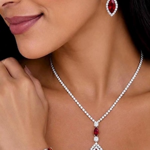 May include: A jewelry set consisting of a necklace, drop earrings, and a bracelet. Each piece features marquise-cut deep red stones surrounded by small clear stones set in a silver-toned metal. The necklace has a central pendant drop design.