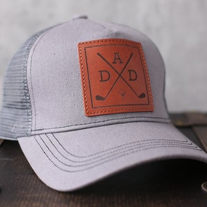 May include: Grey trucker hat with a brown leather patch featuring the letters "ADD" and crossed golf clubs.