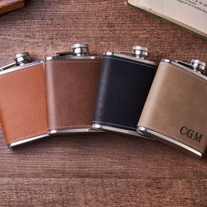 May include: Four leather-covered hip flasks in brown, black, and tan with silver accents. The tan flask has the initials "CGM" engraved on it.