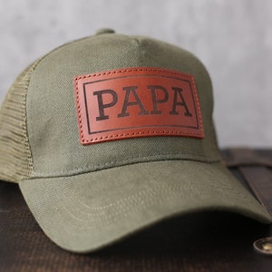 May include: A green and brown trucker hat with a brown leather patch that says "PAPA" in black lettering.