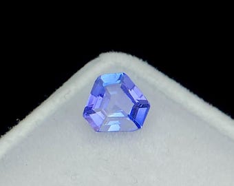 May include: A faceted, blue gemstone with a unique pentagonal shape. The gem has a brilliant cut, reflecting light and showcasing its clarity. The stone is set against a white background, highlighting its color and form. The gem is a striking example of fine jewelry.